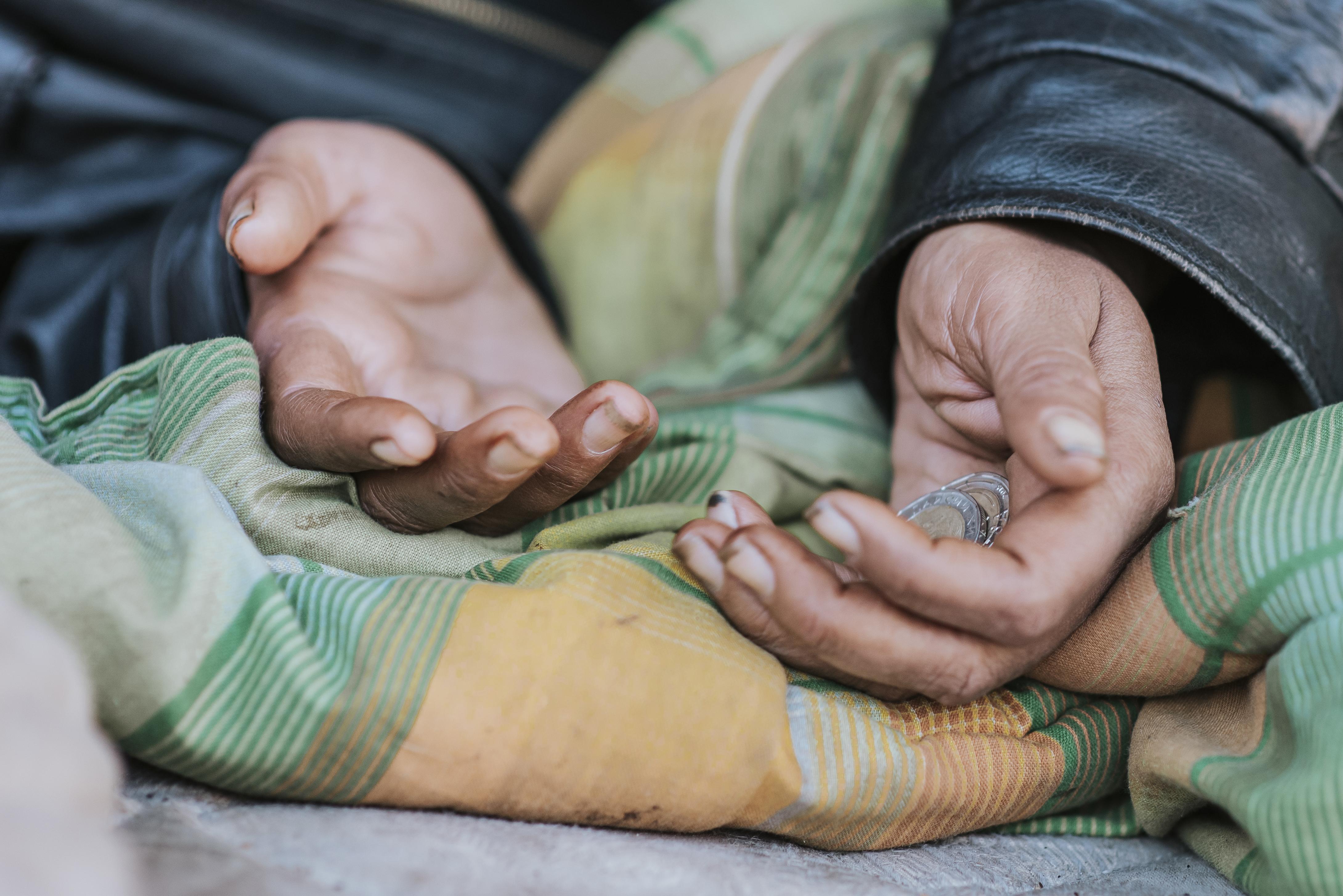 Two hands with tan skin, hugging a pile of money that's between three crumpled green, yellow, and orange fabrics. No clear...